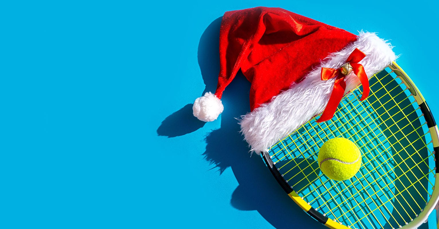 Santa Claus hat on tennis racket with ball on blue background.